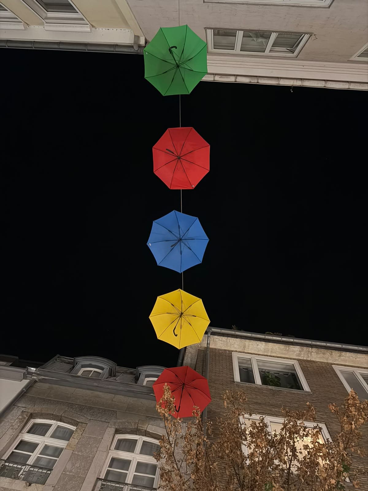 Bunte Schirme hängen an einer Schnur über einer Straße
